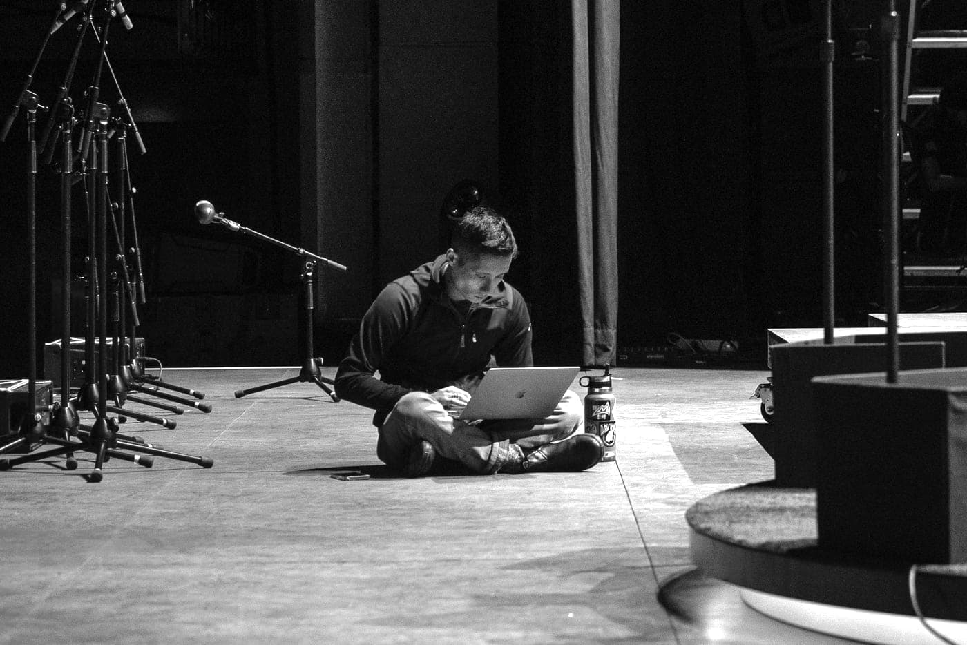 Ezra Zwaeli sitting alone on a stage floor, working on a laptop